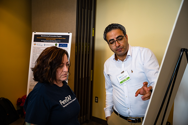 A fellow pointing to his poster while a woman listens