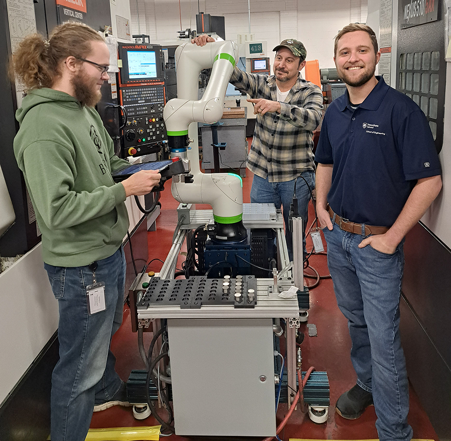 Three men working in a lab on equipment with a large tube and a laptop