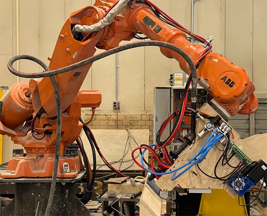 Orange ABB industrial robotic arm fitted with a custom end effector and bundled cables in a workshop setting.
